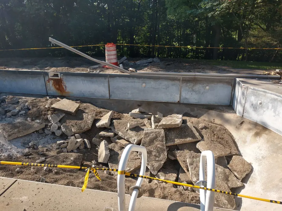 Steel pool wall panel with its skimmer opening, set among broken concrete during a rebuild