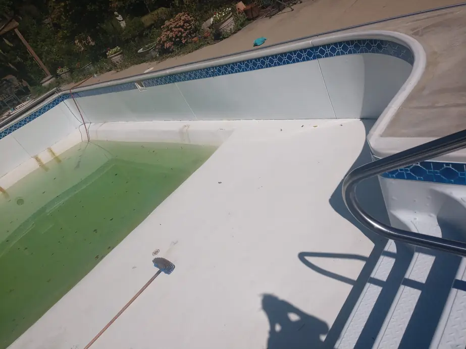 Drained vinyl-liner pool with a blue geometric border tile and a stainless handrail, before renovation